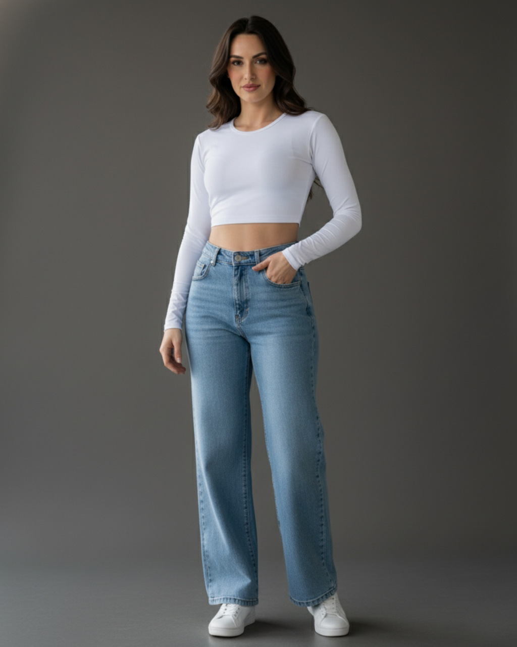 Modelo morena em estúdio vestindo um top cropped branco de manga longa liso com calça jeans larga de cintura alta e tênis brancos. Look casual chic e moderno. Roupa versátil para o dia a dia, moda feminina atual.