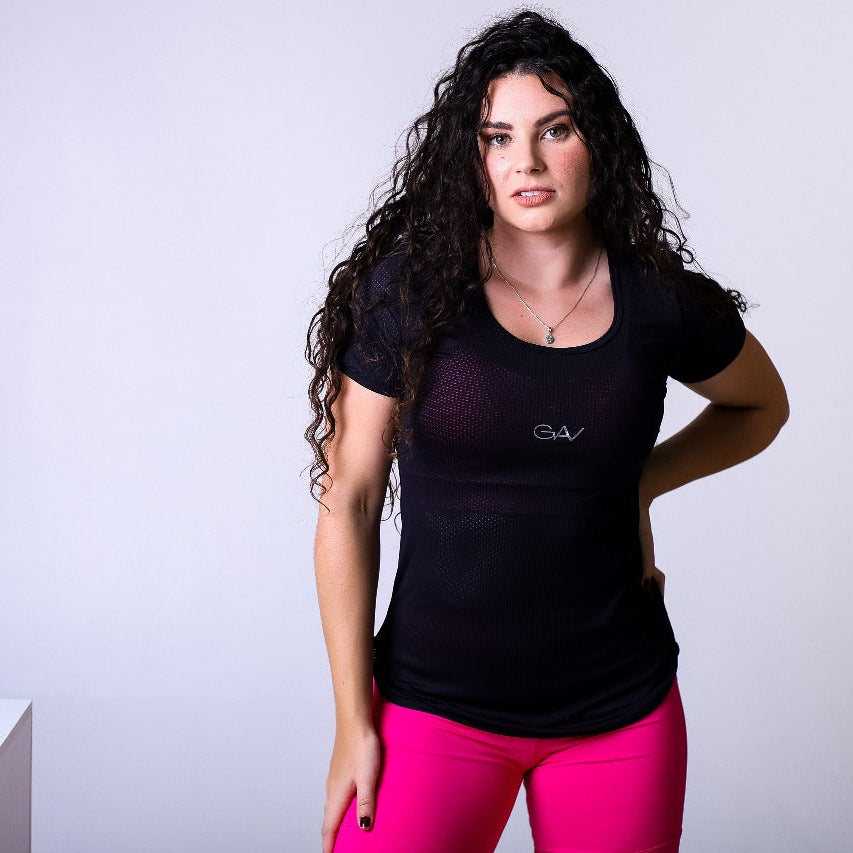 Modelo veste conjunto fitness GAV com blusa preta de tecido mesh transparente e short rosa choque de cintura alta, em fundo de estúdio.