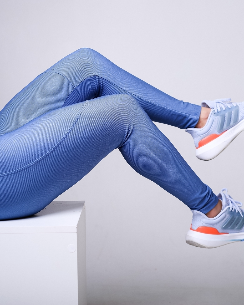 Mulher sentada com pernas esticadas, usando a mesma legging azul. A posição evidencia a elasticidade do tecido e o caimento natural durante o movimento.